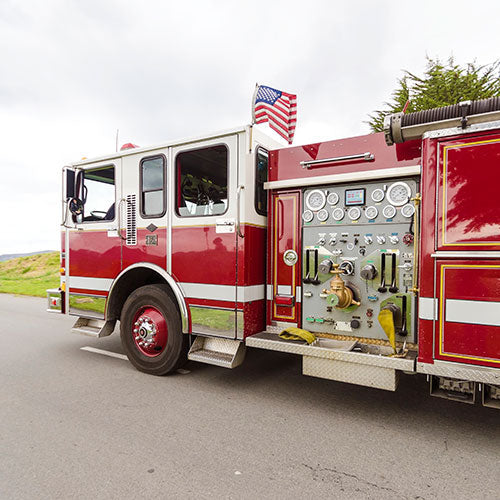 Nylon American Flag - Beacon® displayed flying from a red fire truck parked on a road with a cloudy sky background