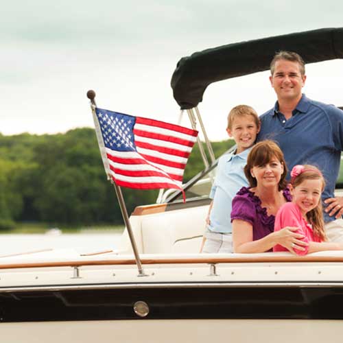 Family of four smiling on a boat with a Nylon American Flag - Beacon® flying on the stern against a natural lake backdrop