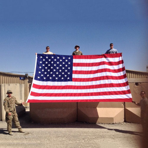 Four military personnel holding a large Nylon American Flag - Beacon® outdoors against a clear blue sky.
