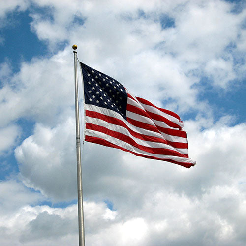 Nylon American Flag - Beacon® flying on a flagpole against a partly cloudy blue sky background.