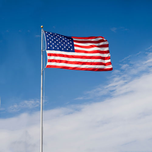 Nylon American Flag - Beacon® flying on a tall flagpole against a bright blue sky with light clouds.
