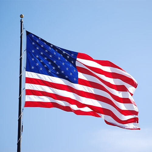 Nylon American Flag - Beacon® waving in the wind against a clear blue sky, displaying vibrant red, white, and blue colors.