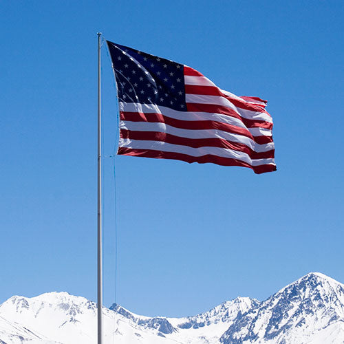 Nylon American Flag - Beacon® flying on a flagpole against a clear blue sky with snow-capped mountains in the background