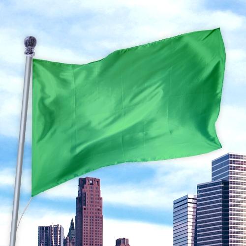Green solid colored flag made of premier nylon waving on a pole against a city skyline and blue sky, Solid Colored Flags - Premier Nylon