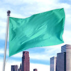 Green flag made of durable nylon fabric waving on a pole above a city skyline, Solid Colored Flags - Premier Nylon