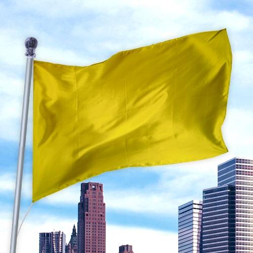 A bright yellow Solid Colored Flags - Premier Nylon fluttering on a silver flagpole against a city skyline under a partly cloudy sky.