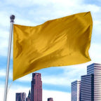 Yellow solid colored flag made of a durable material waving on a pole above city skyscrapers, Solid Colored Flags - Premier Nylon.