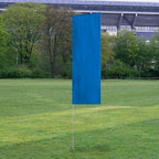 Solid Tall Advertising Flags with a plain blue design standing upright on a metal pole in a grassy outdoor area with trees and a stadium in the background