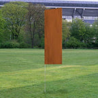 Solid Tall Advertising Flags with a solid rust-colored design displayed outdoors on a grassy field near trees and a stadium.