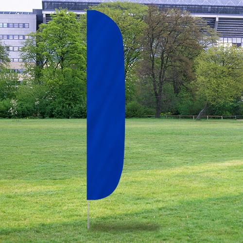 Solid Color Flutter Flags in vibrant blue positioned outdoors on green grass with trees and buildings in the background.