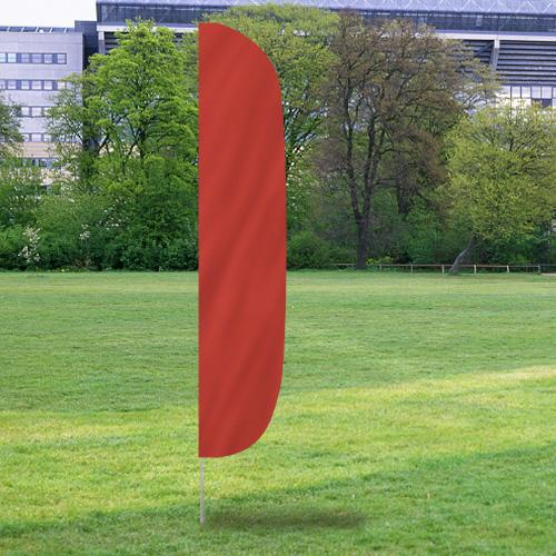 Solid Color Flutter Flags in bright red displayed outdoors on a grassy field with trees and buildings in the background.