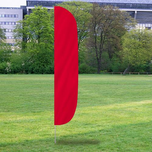 Red solid color flutter flag standing upright on a grassy field with trees and buildings in the background, showcasing Solid Color Flutter Flags.