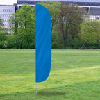 Tall solid bright blue outdoor banner fluttering on a pole in a park setting featuring Solid Color Flutter Flags.