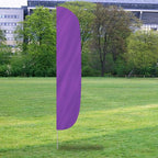 Solid Color Flutter Flags in vibrant lavender purple displayed outdoors on a grassy field with trees and buildings in the background.