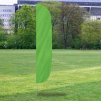 Solid Color Flutter Flags in bright green displayed outdoors on a grass field with trees and buildings in the background.