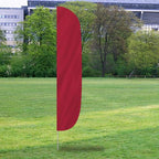 Solid Color Flutter Flags in deep red standing on a grassy field with trees and buildings in the background