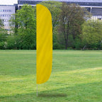 Bright yellow Solid Color Flutter Flags standing upright on a green grassy field with trees and buildings in the background