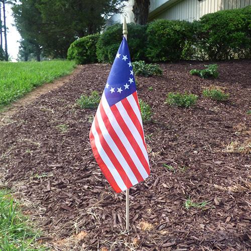 Betsy Ross 13-star American stick flag displayed outdoors in landscaped area